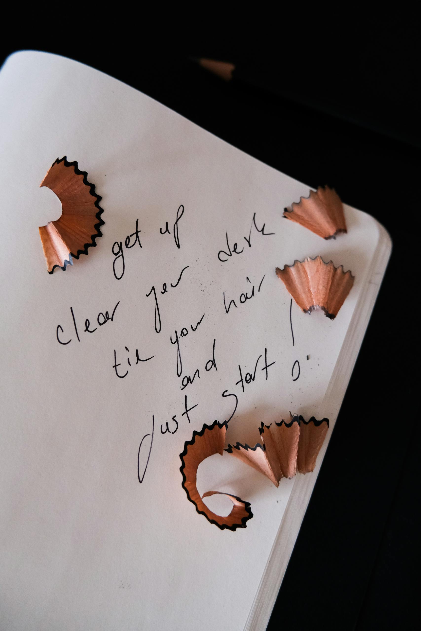 Handwritten message with pencil shavings on open notebook, inspiring start and motivation.
